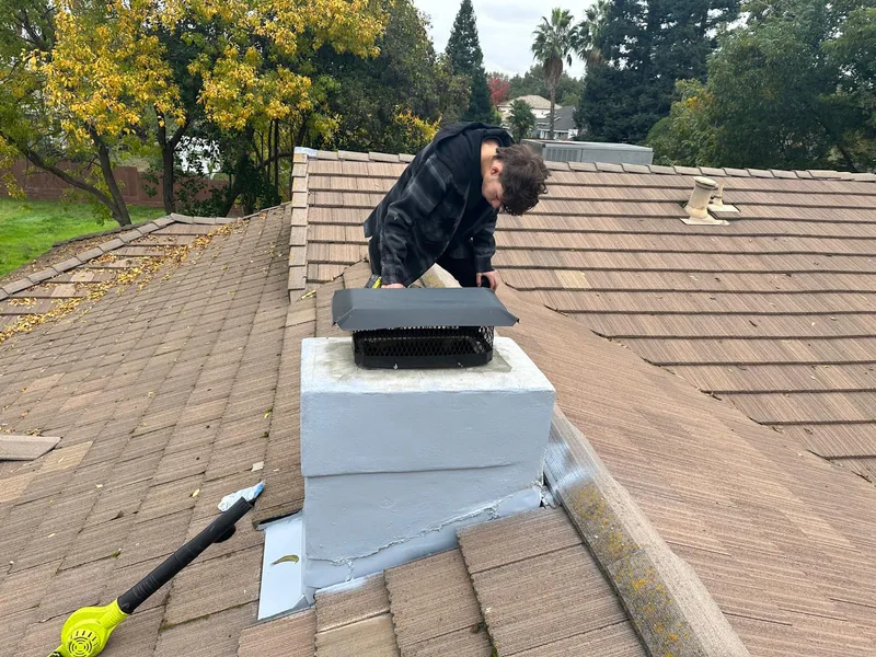 CSIA certified technician inspecting a chimney crown and cap from a tile roof during a Level 2 chimney inspection
