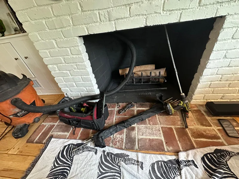 Open masonry firebox with sweep rods and HEPA vacuum in place while diagnosing a fireplace draft problem