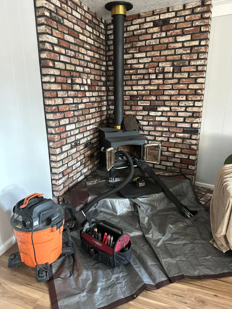 Wood stove and connector pipe being serviced with tarps and a HEPA vacuum after warning signs were reported